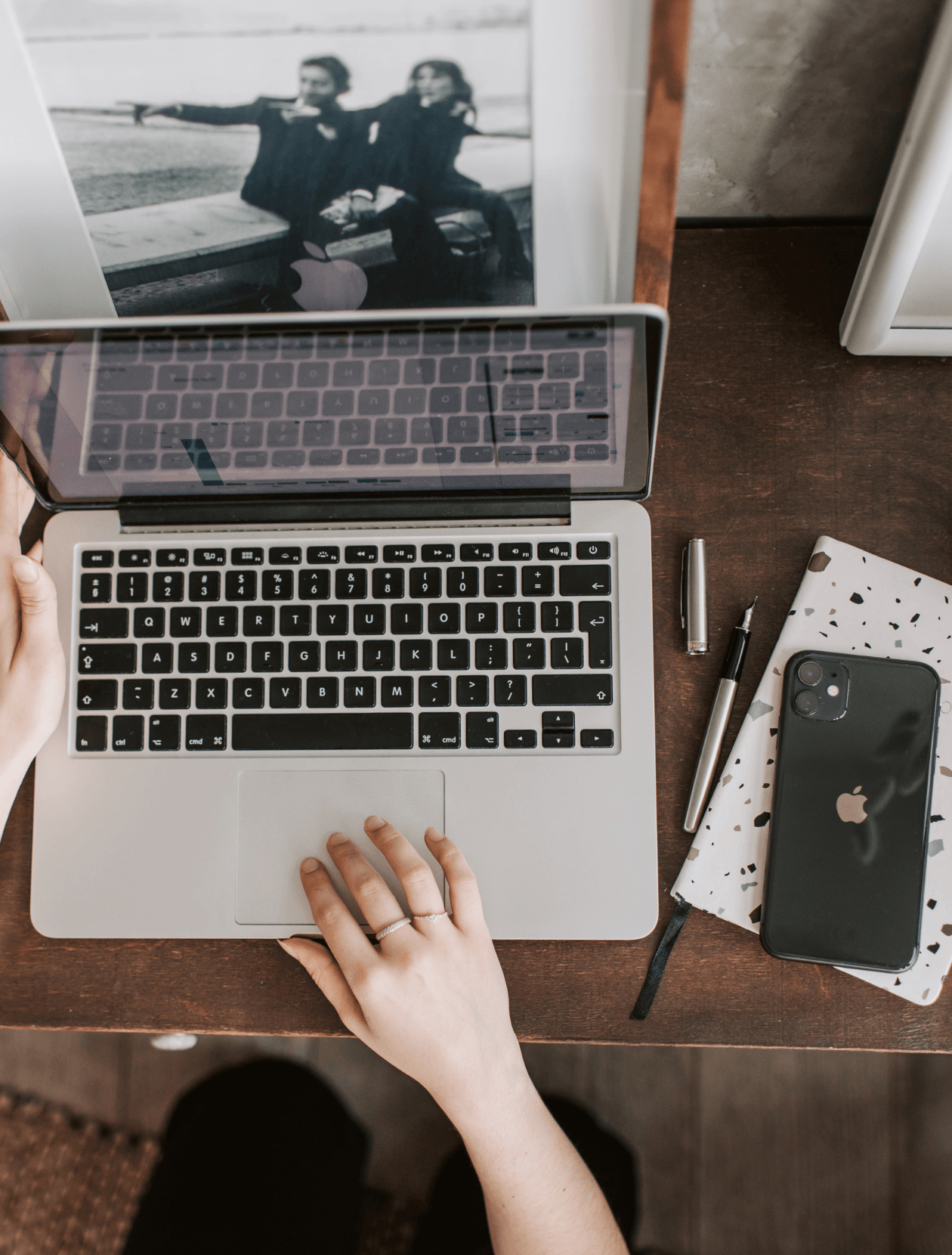 someone using a Macbook laptop with phone and notepad visible